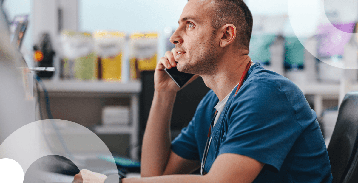 Healthcare worker in blue scrubs on the phone at desk